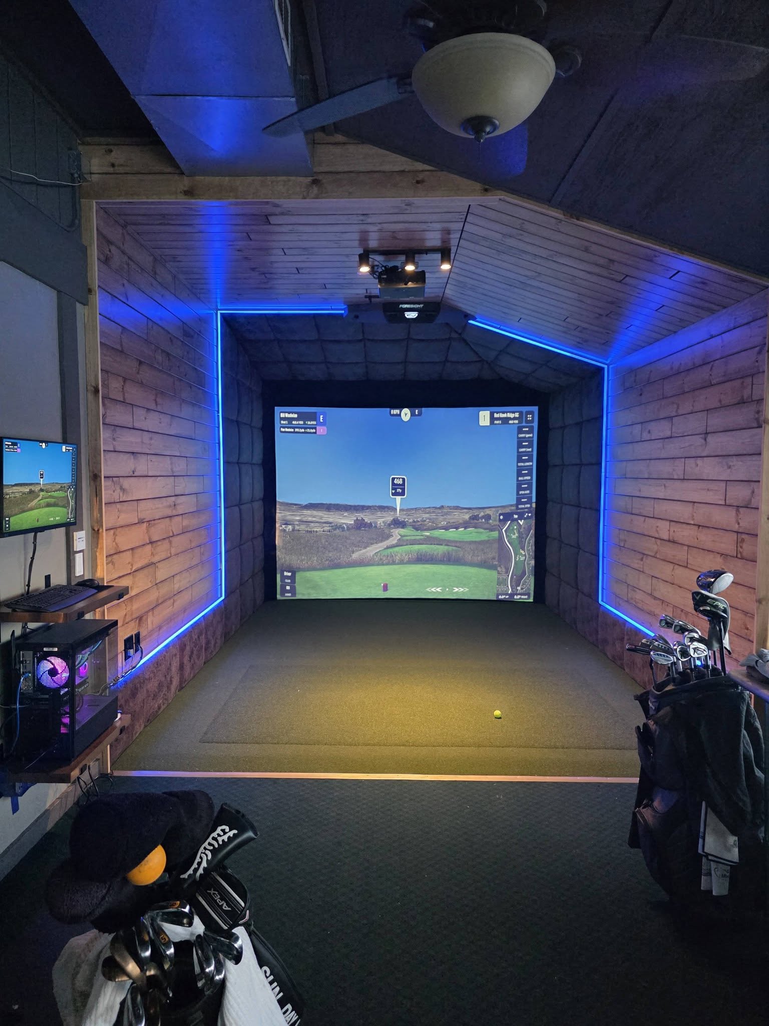 Reclaimed barnwood home golf simulator room with blue LED cove lighting