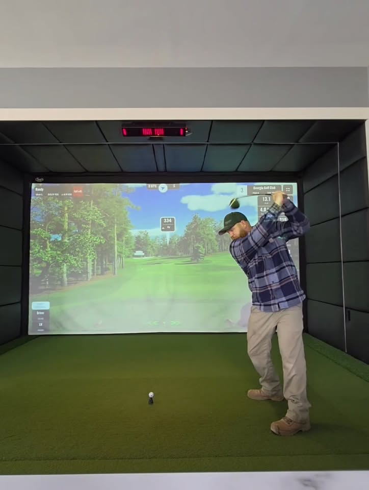 Golfer swinging in a modern black acoustic-panel simulator enclosure